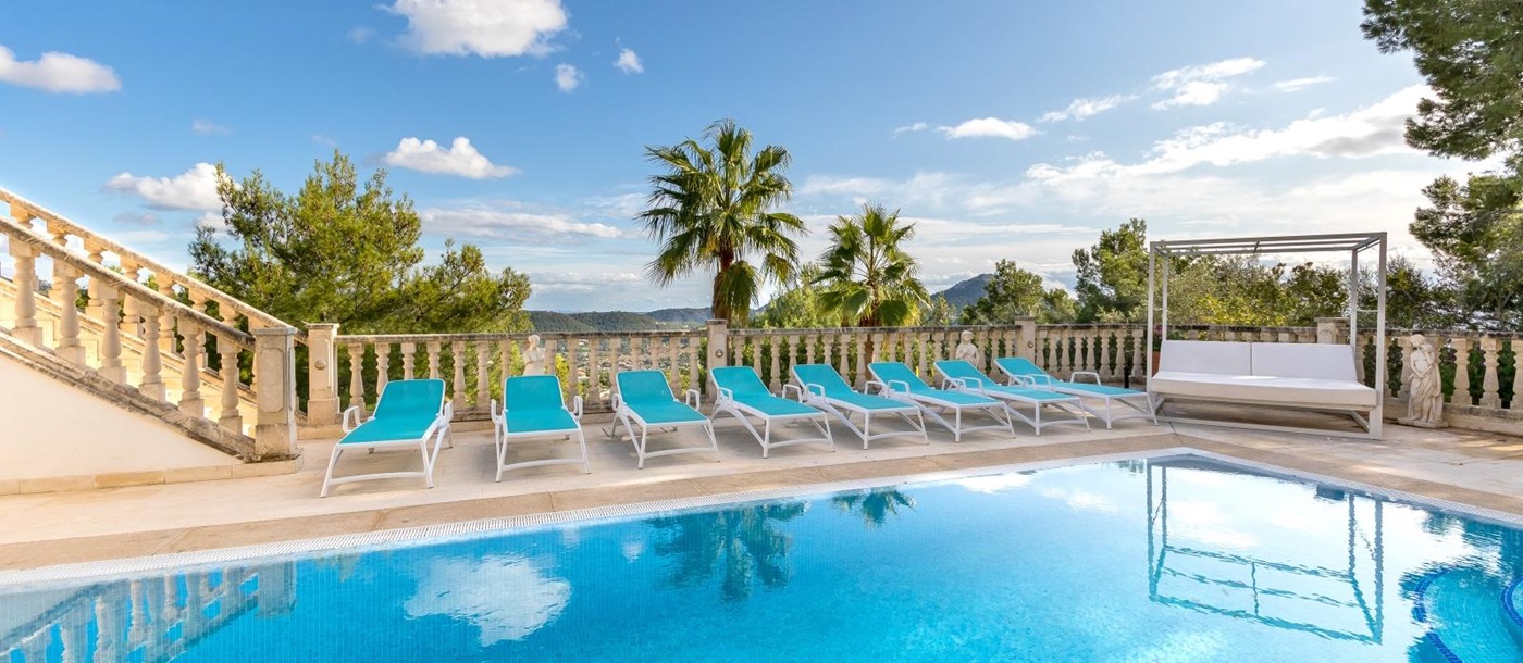 Pool area with sun loungers, day bed, palm trees and mountain view at Casa Verano in Mallorca, Spain