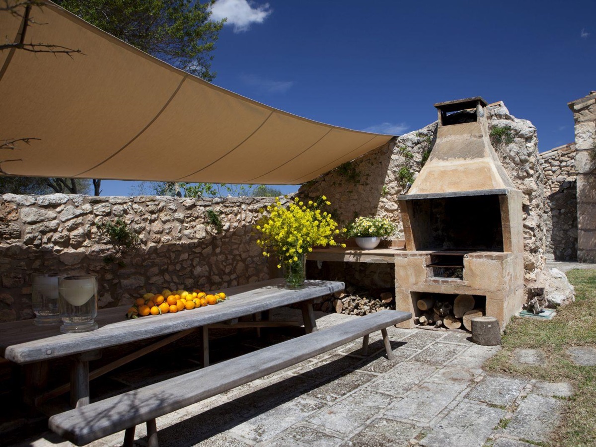 Long wooden table and bench on paved area in front of brick built BBQ at villa San Lorenzo in Mallorca