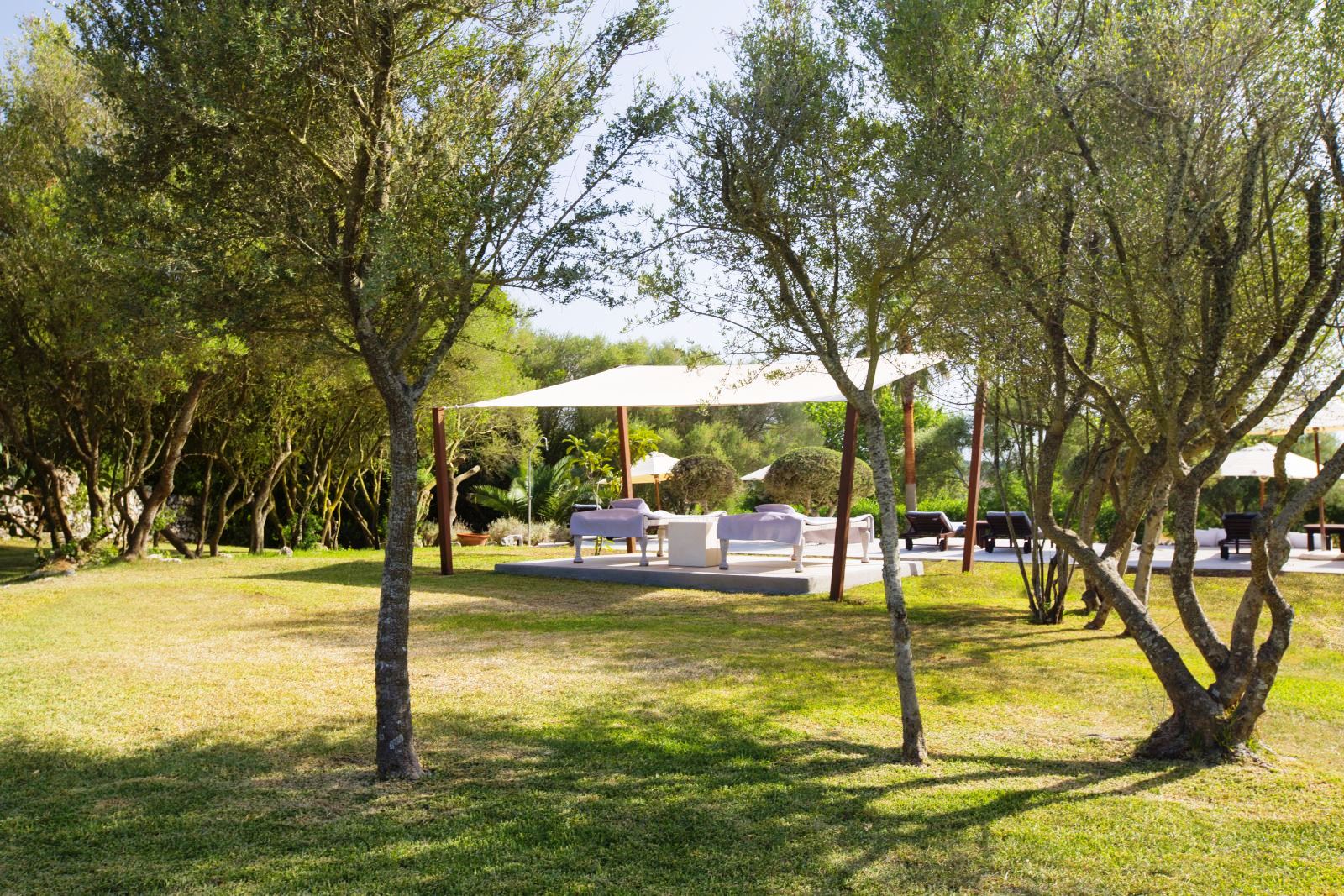 Platform with 2 white sunbeds under a white canopy amongst trees in the garden at villa San Lorenzo in Mallorca