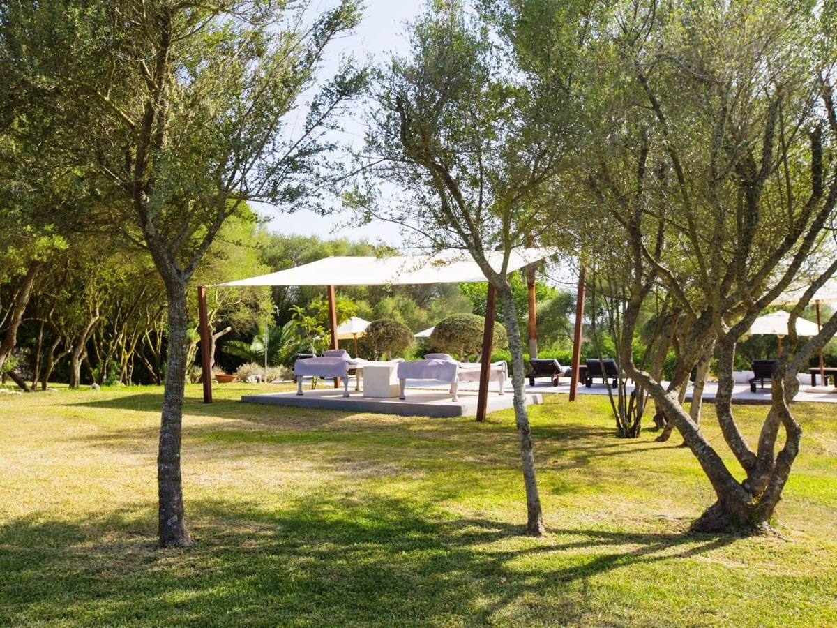 Platform with 2 white sunbeds under a white canopy amongst trees in the garden at villa San Lorenzo in Mallorca