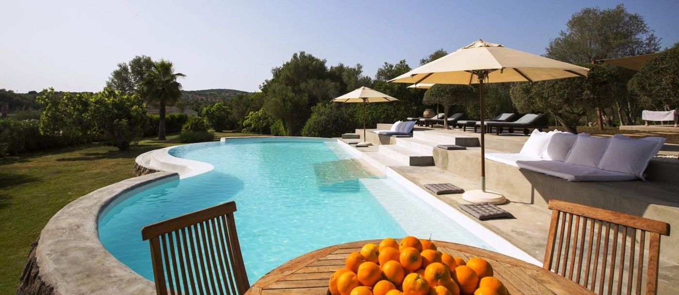 Curved swimming pool with pool furniture and table with big bowl of oranges at villa San Lorenzo in Mallorca