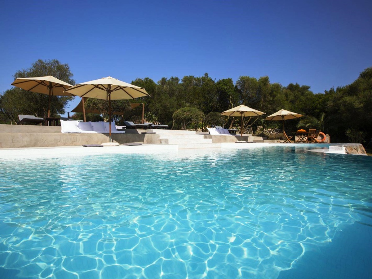 Swimming pool with trees in the background sun umbrellas and pool furniture at villa San Lorenzo in Mallorca