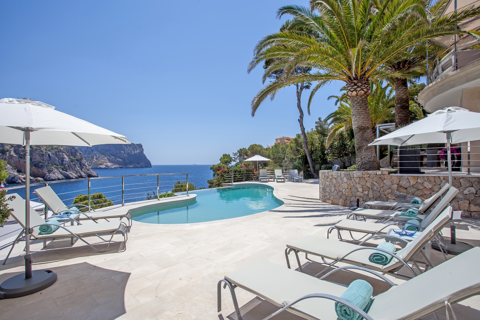 Pool and pool area with sea view, sun loungers, umbrellas, fresh towels and palm tree at Vista Marmessen in Mallorca, Spain