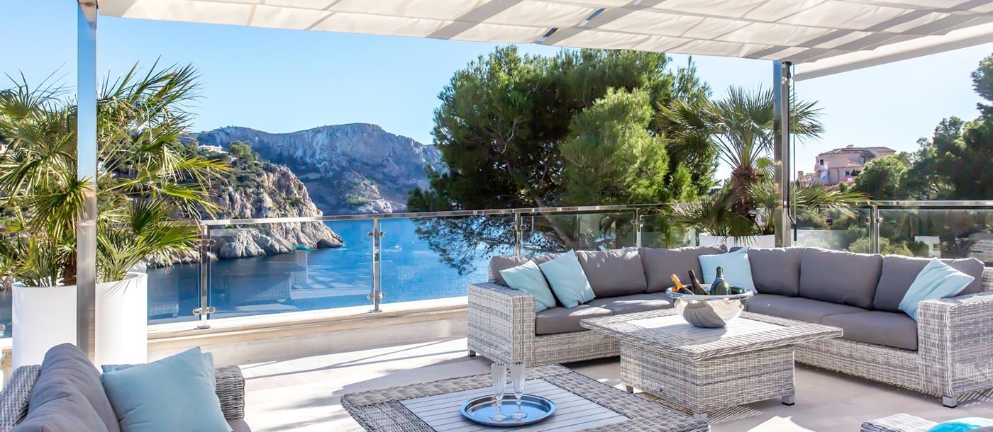 Covered terrace with long sofas, coffee tables, plants and sea view at Vista Marmessen in Mallorca, Spain