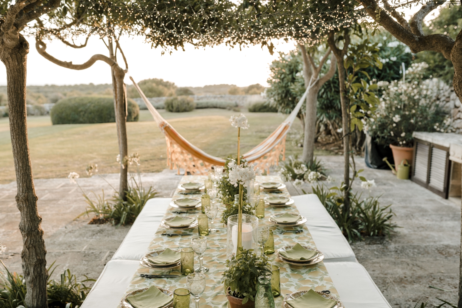 Outdoor dining area under a canopy of fairy lights with views over a hammock and the gardens at Menorcan luxury villa Binicalaf