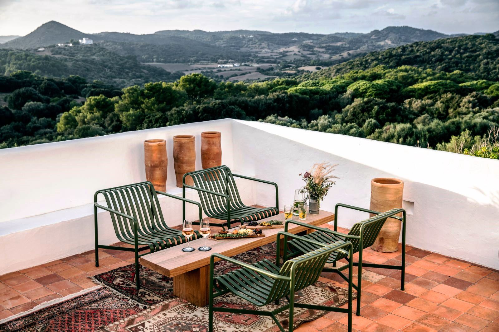 four green chairs and a long table with food and wine on the roof terrace at luxury villa Casa Benedicta in Menorca 