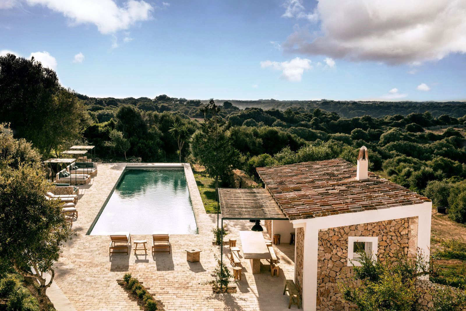 view over the pool and pool house four green chairs and a long table with food and wine on the roof terrace at luxury villa Casa Benedicta in Menorca 