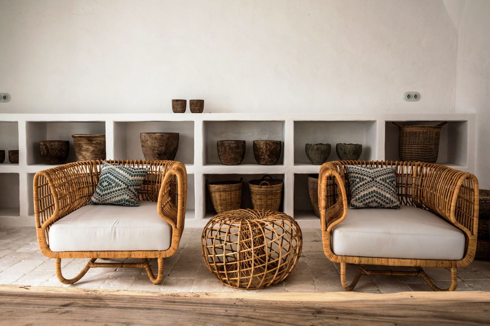 two wicker chairs with white cushions with baskets behind four green chairs and a long table with food and wine on the roof terrace at luxury villa Casa Benedicta in Menorca 