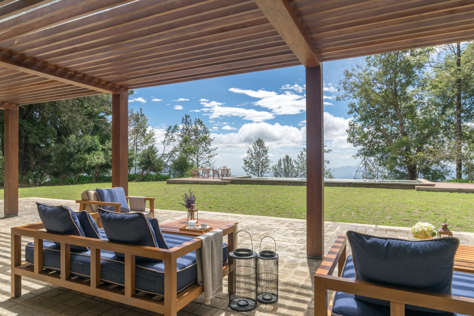A sofa and chairs with comfy blue cushions and a coffee table undercover of a wooden roof on the patio at Goatfell hotel, a former tea planter’s bungalow