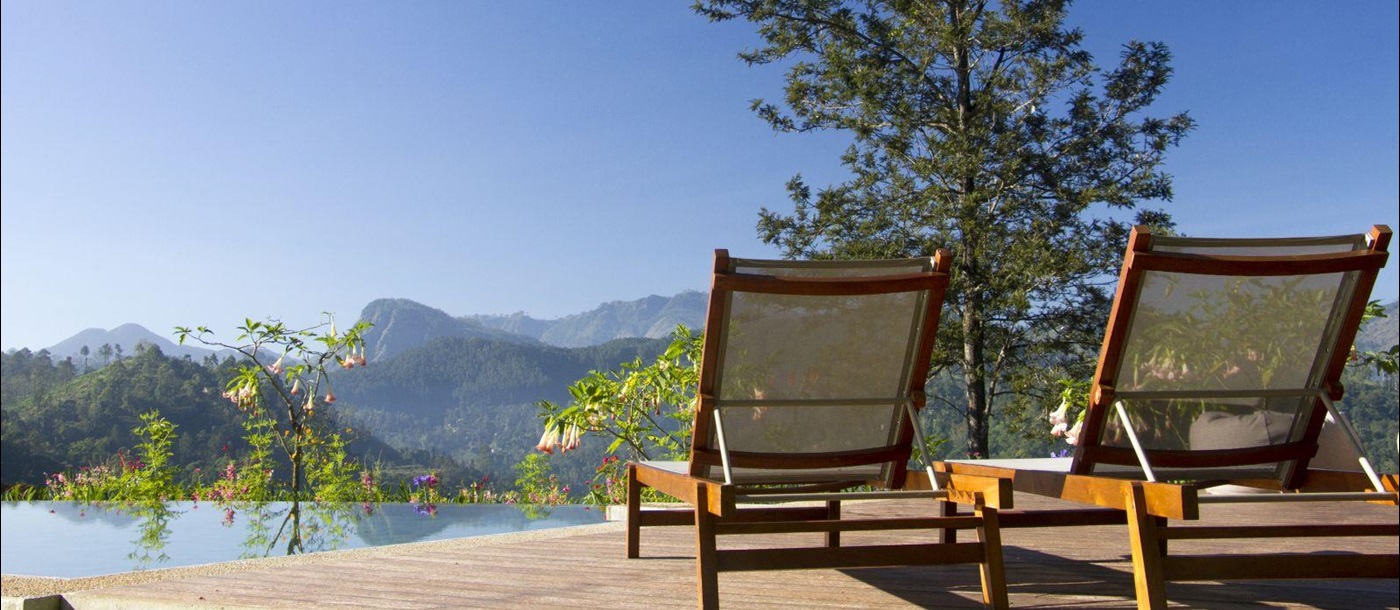 Two sunloungers on a sun deck surrounded by trees and flowers with mountains in the background at Nine Skies in Sri Lanka