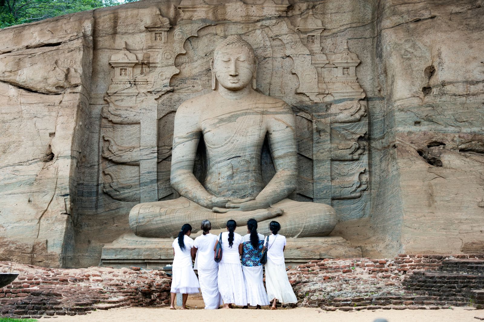 Sri Lankan visitors in traditional dress in front of towering buddha in Polonnaruwa