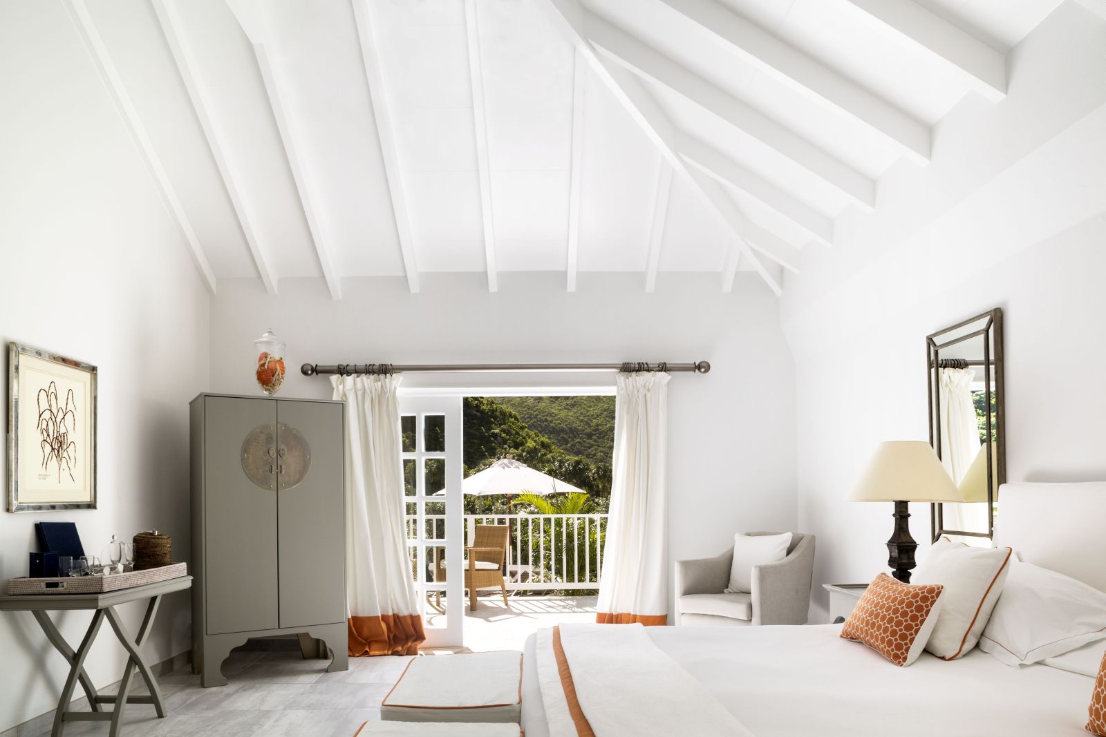 A bedroom decorated in white with a deck overlooking the garden at Hotel Cheval Blanc in St Barths