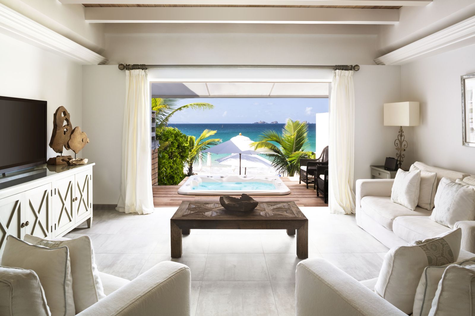 A living room suite with white furniture with a view out onto the beach at Hotel Cheval Blanc in St Barths