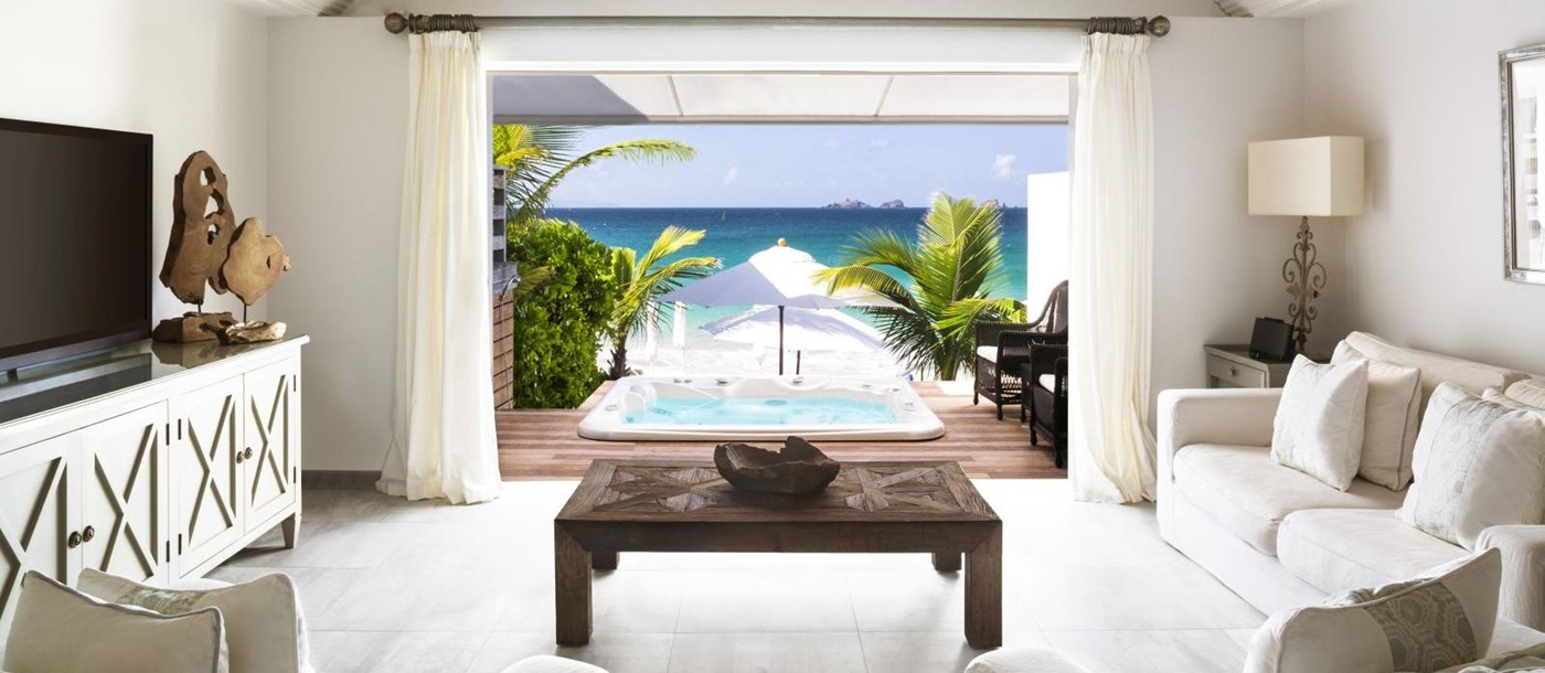 A living room suite with white furniture with a view out onto the beach at Hotel Cheval Blanc in St Barths