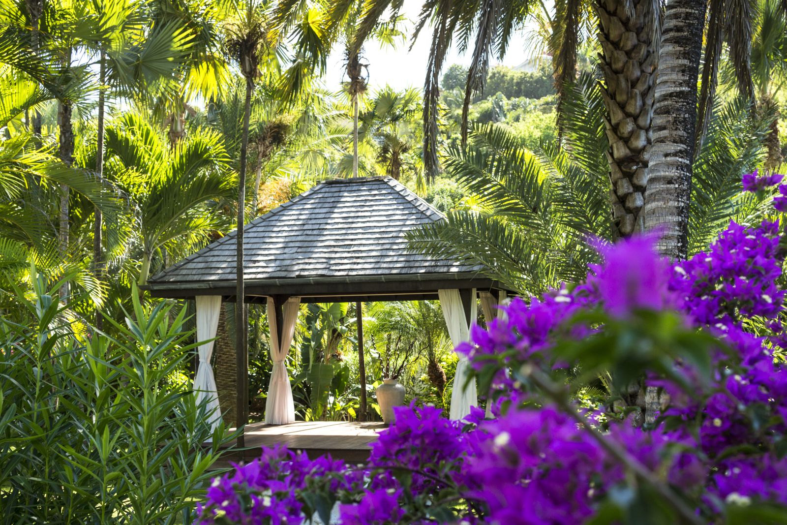 A square pavillion in the gardens at Hotel Cheval Blanc in St Barths surrounded by lush tropial trees and purple flowers