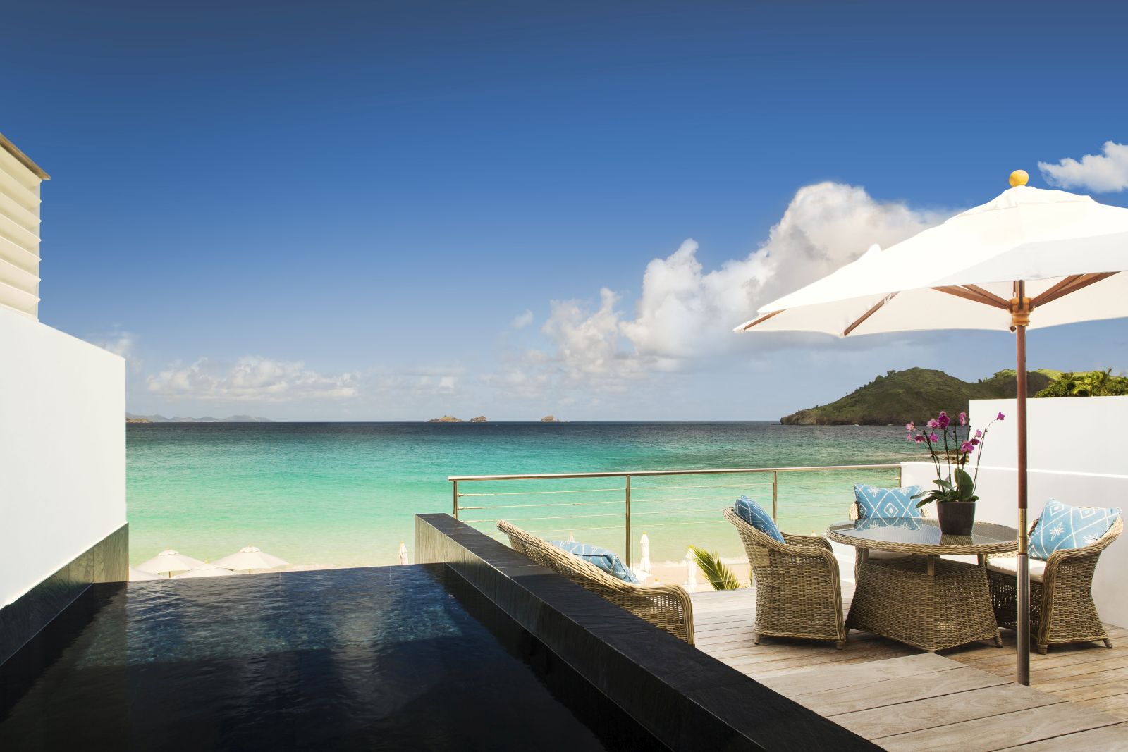 A sun terrace with wicker chairs and a table with sun umberalla overlooking the beach at Hotel Cheval Blanc in St Barths