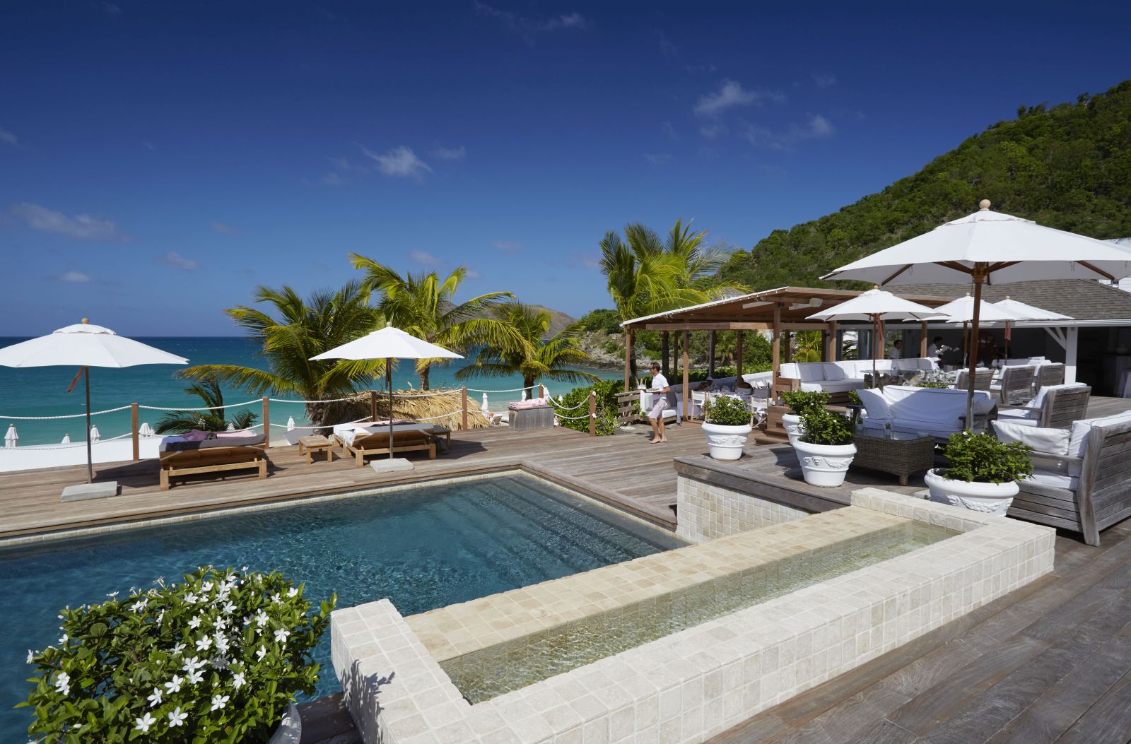 The white bar at Hotel Cheval Blanc in St Barths with chairs, tables and sun umberellas around a pool