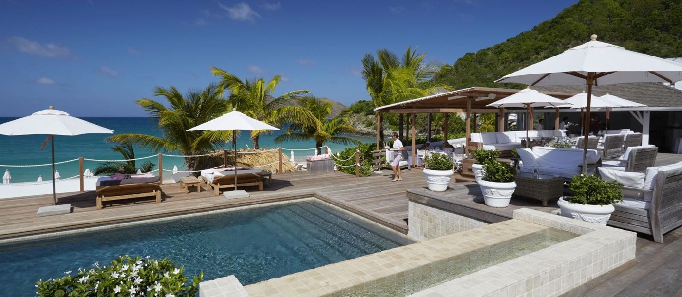 The white bar at Hotel Cheval Blanc in St Barths with chairs, tables and sun umberellas around a pool