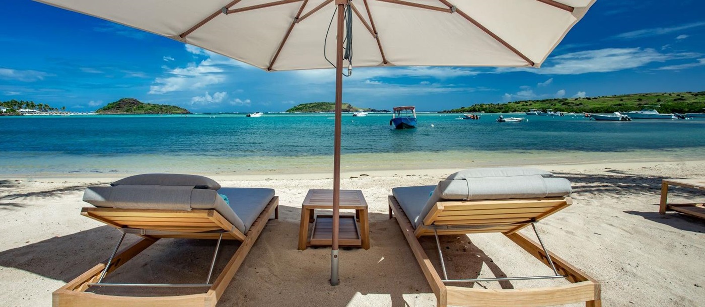 Two sun loungers under a sun umberella on the beach at Le Barthelemy Hotel & Spa in St Barths