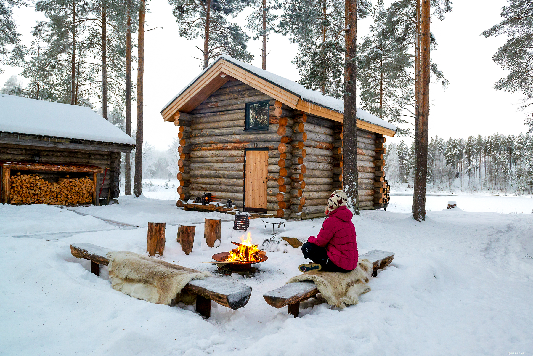 A woman sat by the campfire outside of a cabin at Arctic Retreat in Swedish Lapland