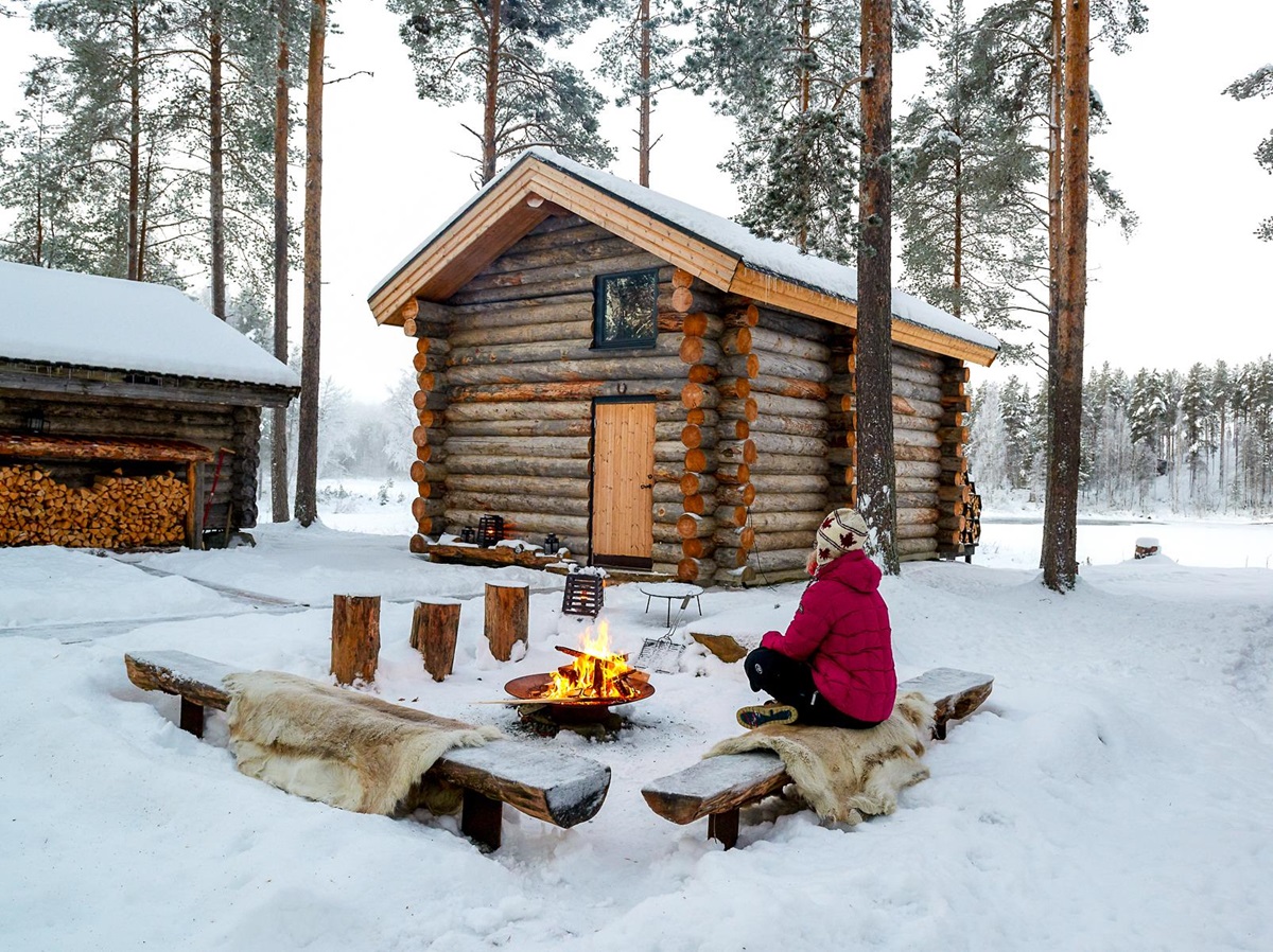 A woman sat by the campfire outside of a cabin at Arctic Retreat in Swedish Lapland