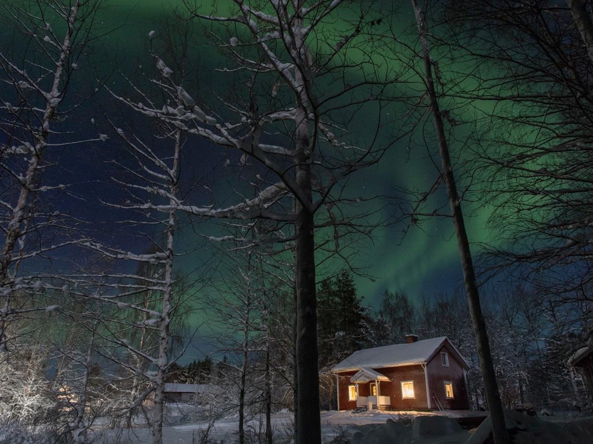 The Northern Lights playing in the sky over the reception house at Aurora Safari Camp in Sweden