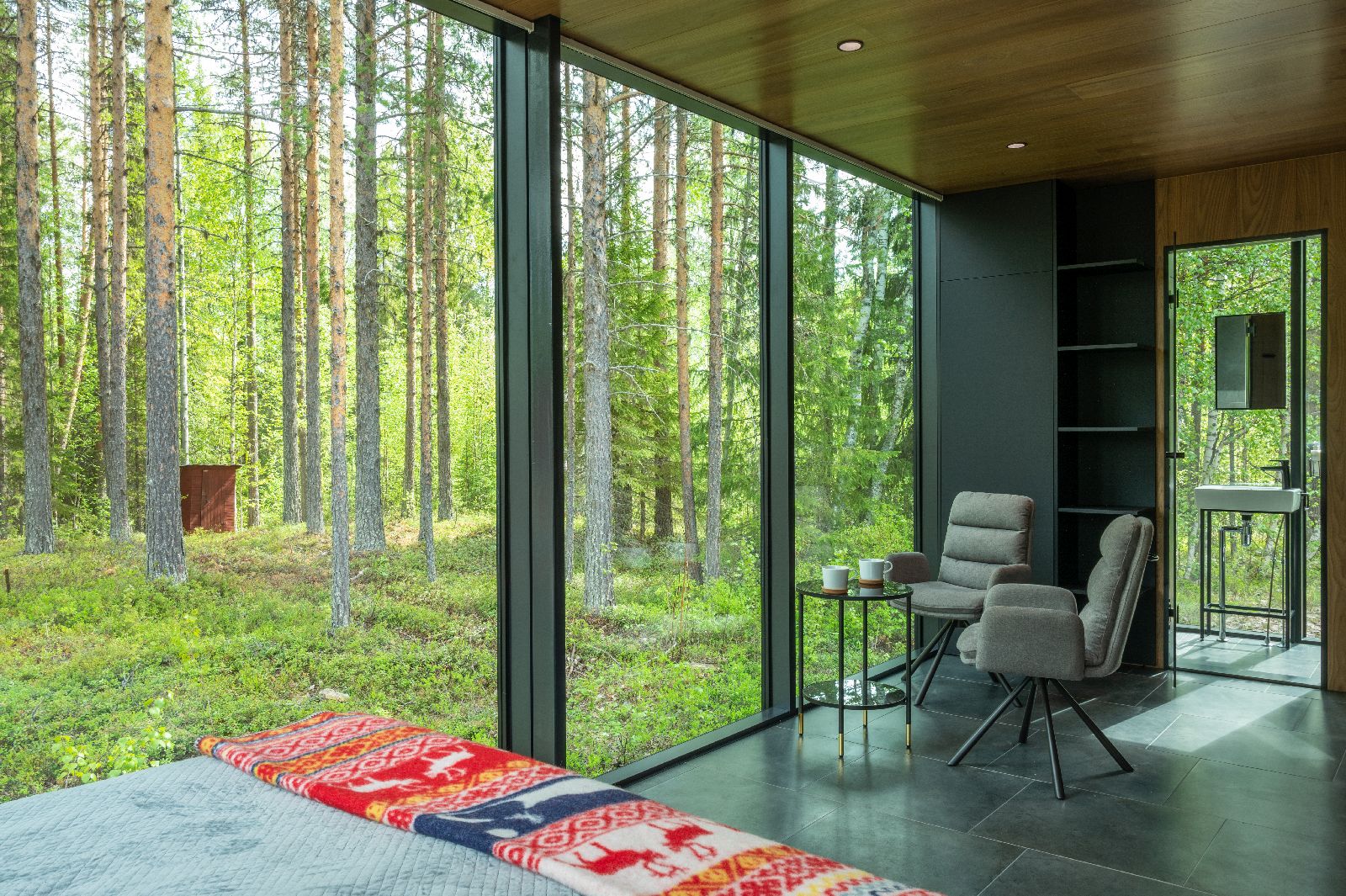 Intimate bedroom with floor to ceiling windows and forest views at luxury Loggers Lodge hotel in Sweden