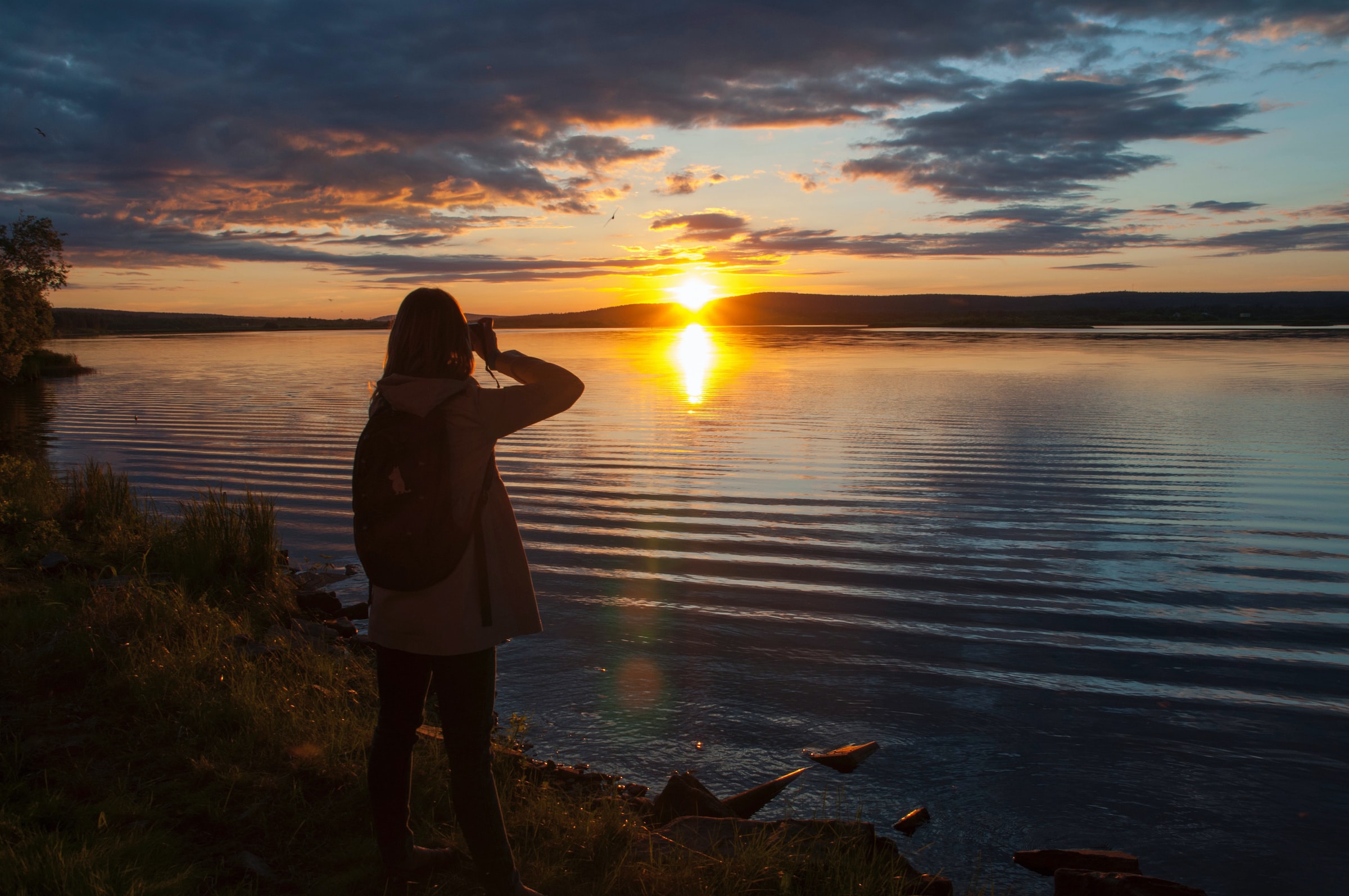 Woman taking a photo of the midnight sun in Lapland, Sweden