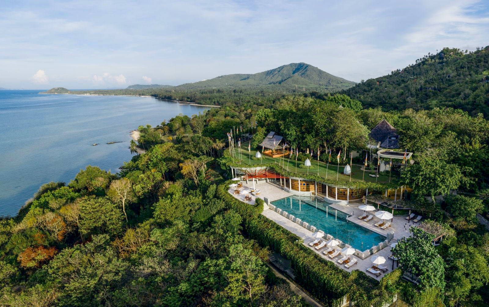 Aerial view over the lap pool with loungers and parasols, the lush gardens and the sea at at luxury wellness resort Kamalaya in Thailand