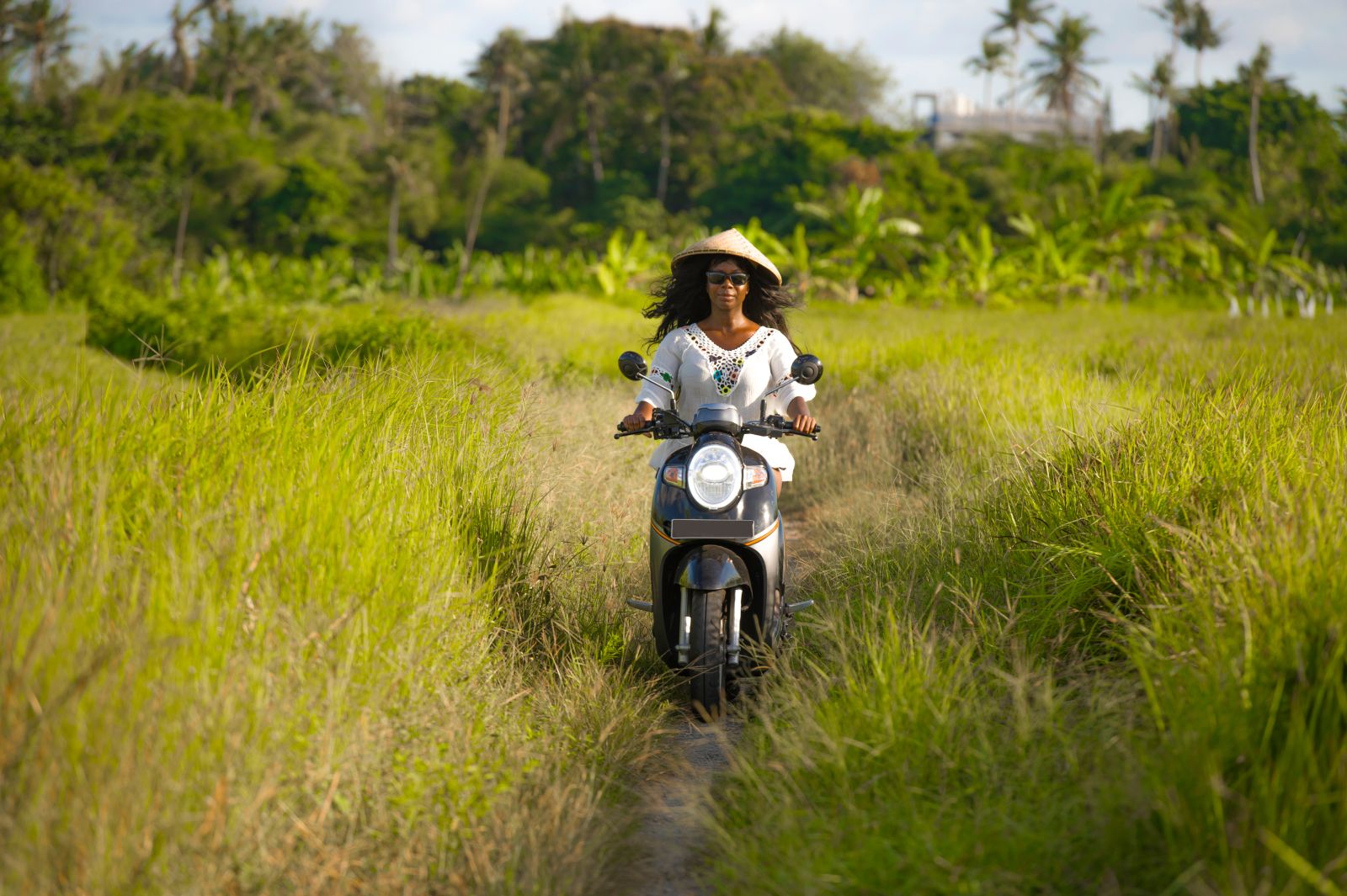 Lady travelling by Vespa through rural scenery in Thailand