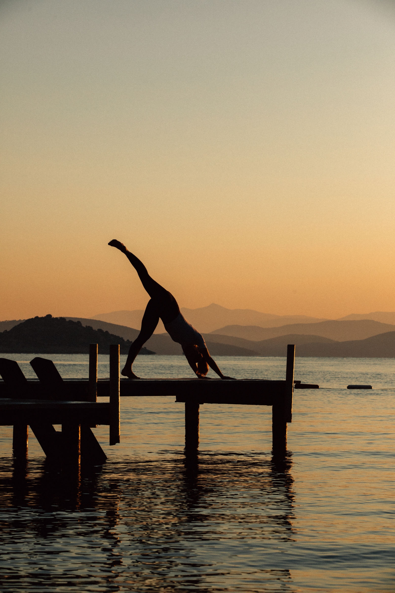 Woman doing a three legged dog yoga pose on a jetty at sunset at luxury hotel Amanruya, Turkey