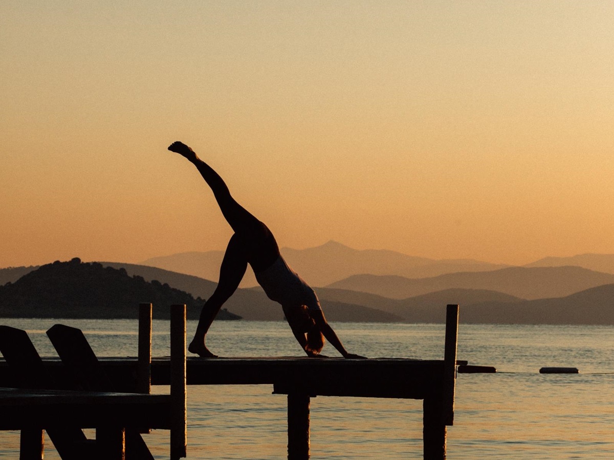 Woman doing a three legged dog yoga pose on a jetty at sunset at luxury hotel Amanruya, Turkey