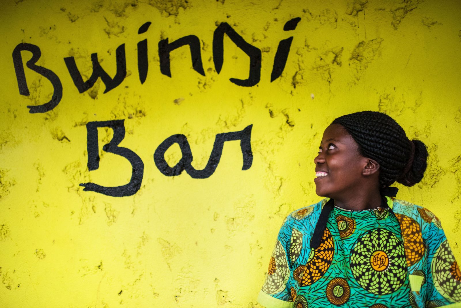 The Bwindi Bar sign on a yellow background with a local african lady looking at it.