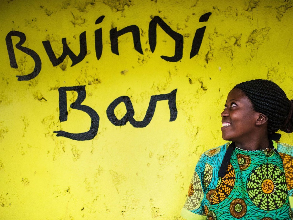 The Bwindi Bar sign on a yellow background with a local african lady looking at it.