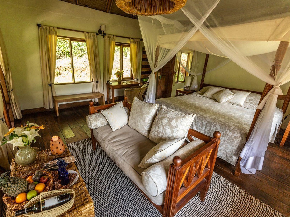 The living are in a bedroom at Bwindi Lodge in Uganda with a couch at the foot of a four poster bed.