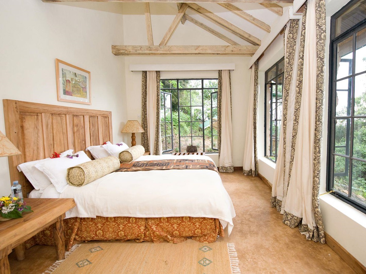 A bedroom with panoramic views from large windows at the foot of the bed at Clouds Mountain Gorilla Lodge in Uganda