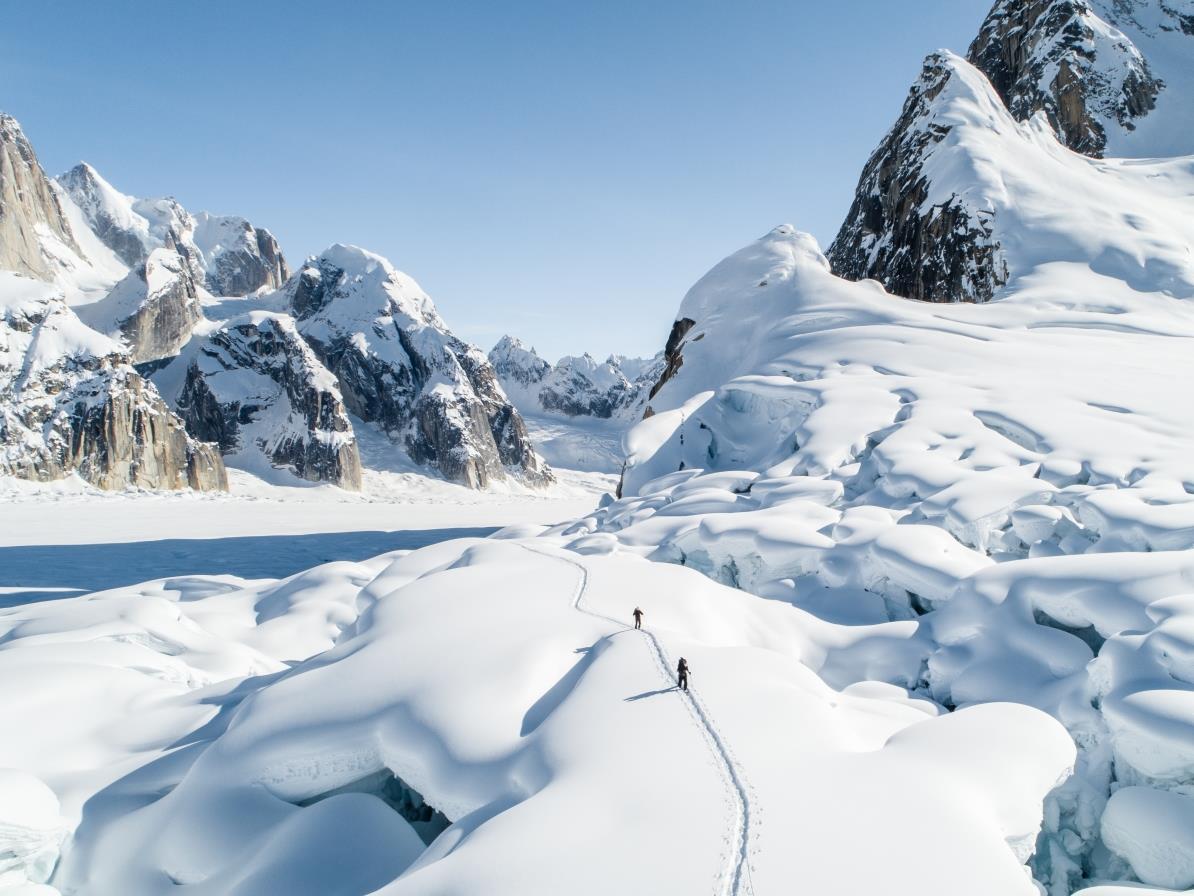 Hikers making their way through thick snow with mountains on either side
