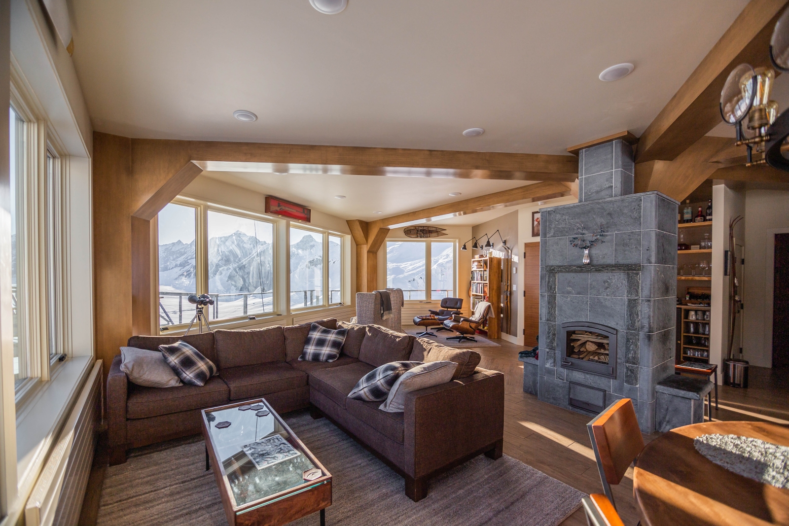 Wooden living area with sofas and fireplace, mountains can be seen through the windows