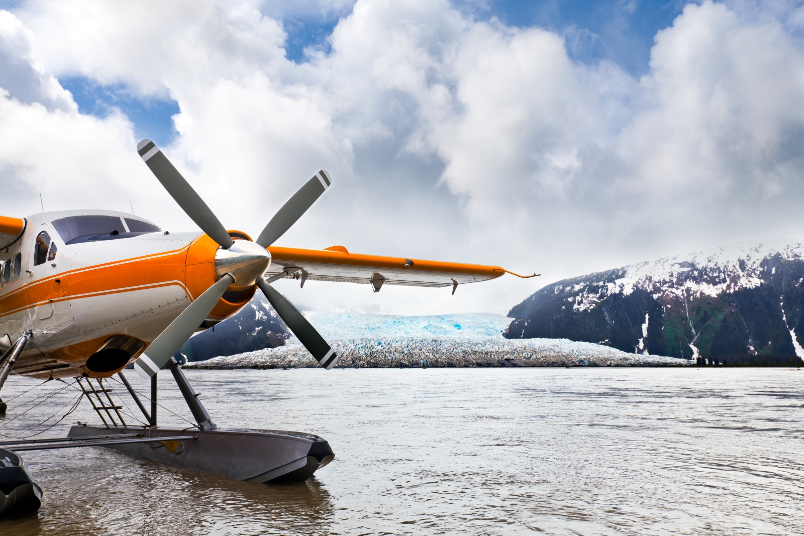 Orange seaplane on water with a glacier in the background