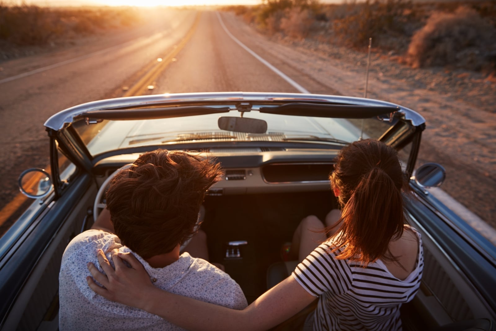 A couple driving into the sunset in a convertible car