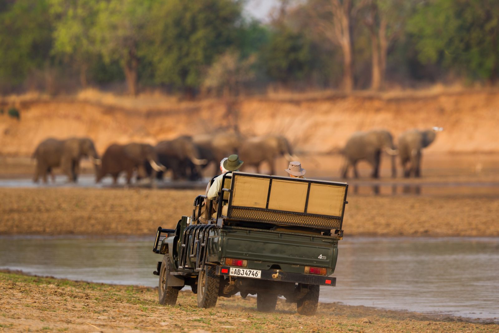 Game Drive vehicle watching elephants by the water at luxury safari camp Luwi Bush Camp in Zambia