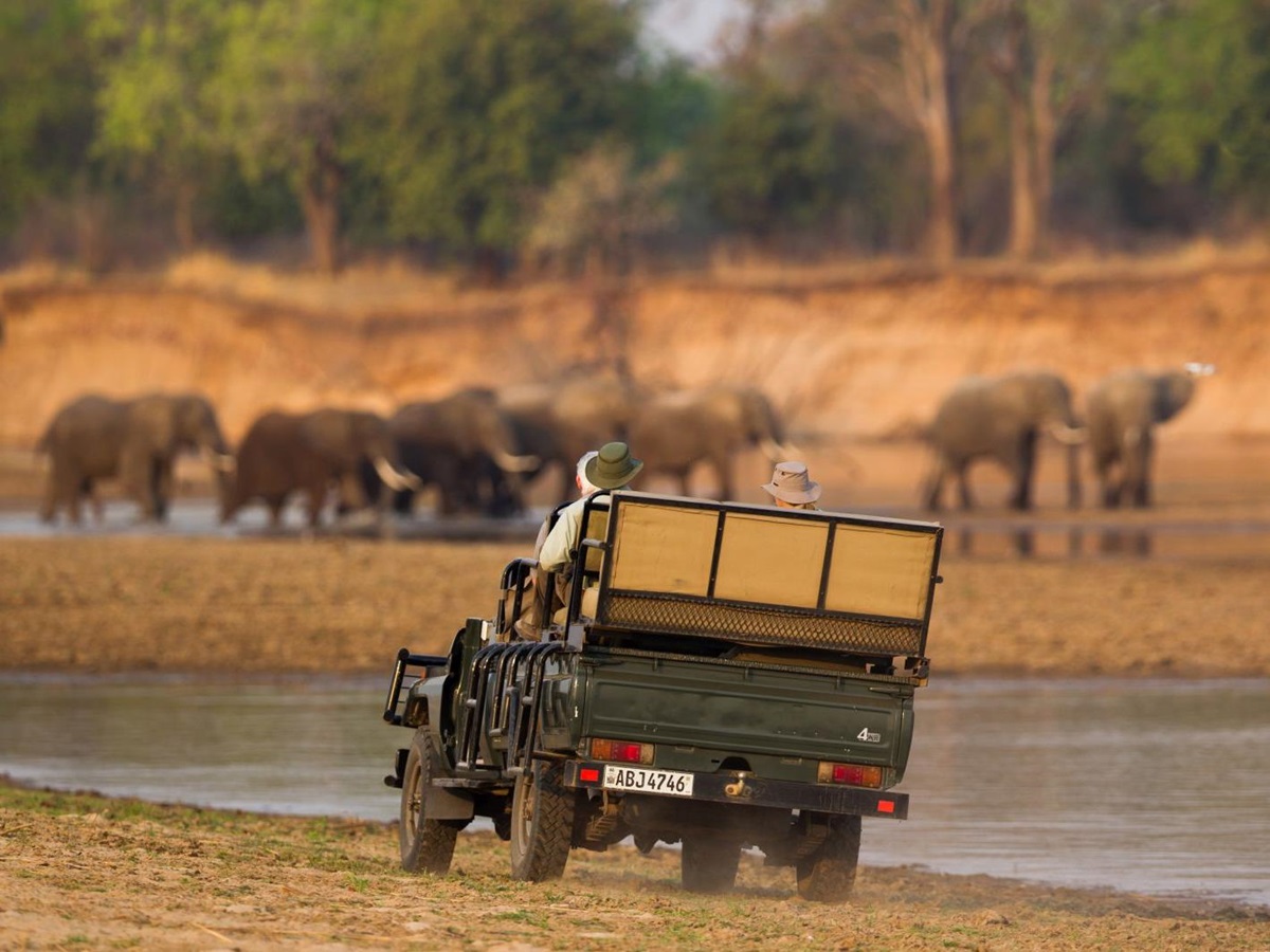 Game Drive vehicle watching elephants by the water at luxury safari camp Luwi Bush Camp in Zambia