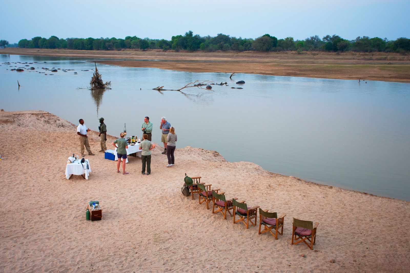 Guests enjoying sundowners by the river during a stay at luxury safari camp Luwi Bush Camp in Zambia