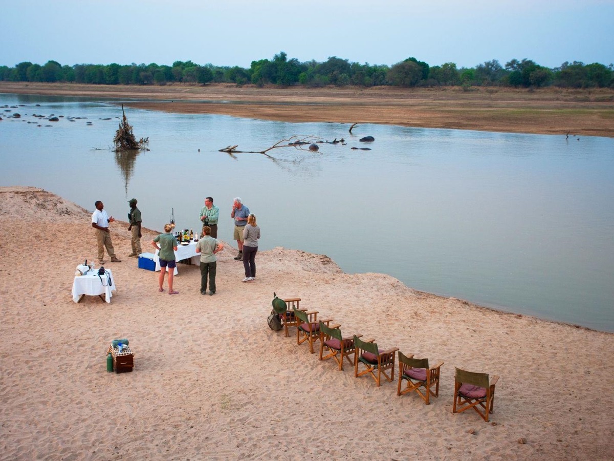 Guests enjoying sundowners by the river during a stay at luxury safari camp Luwi Bush Camp in Zambia