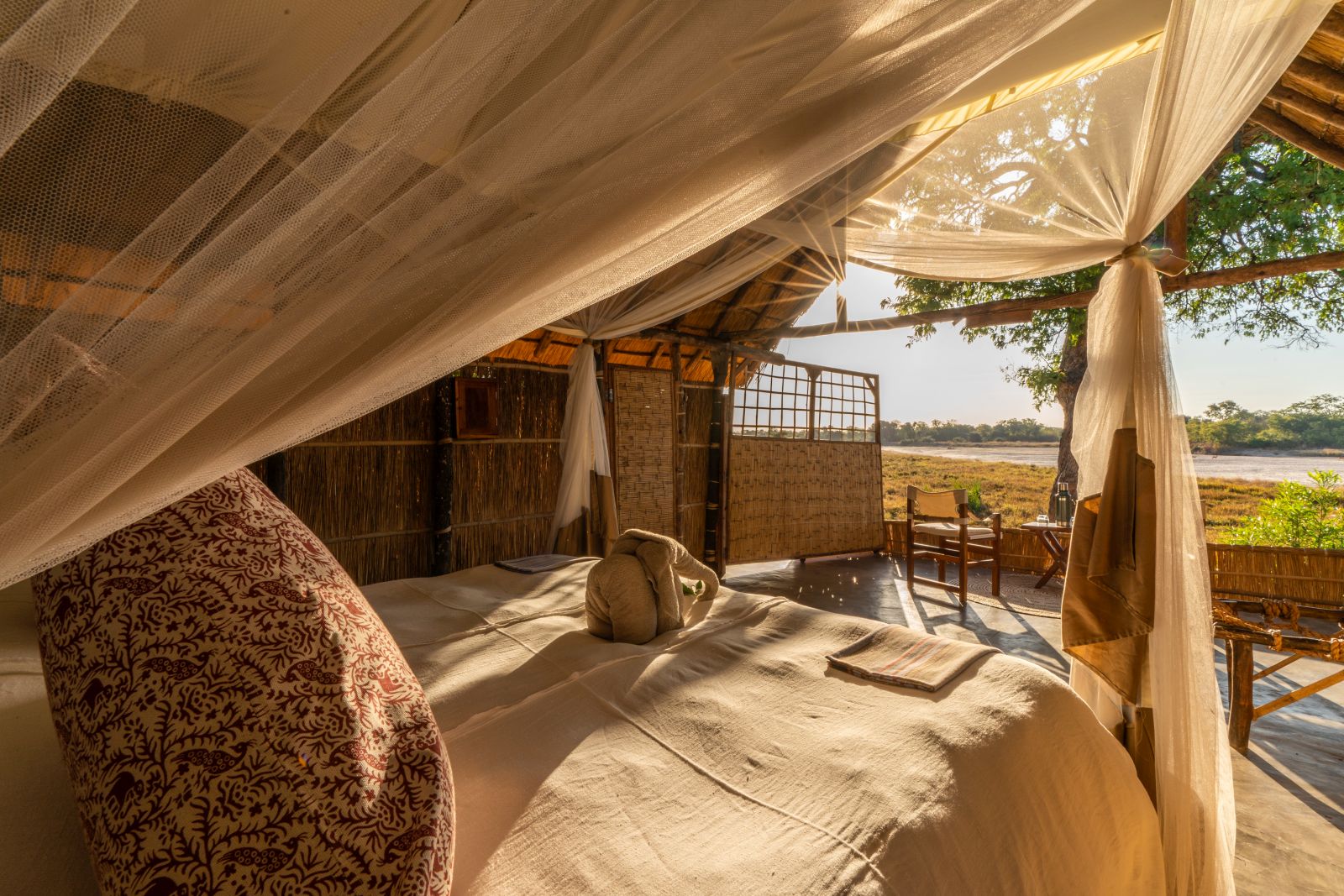 View from the double bed of a thachted room at luxury safari camp Luwi Bush Camp in Zambia over the private terrace and surroundings