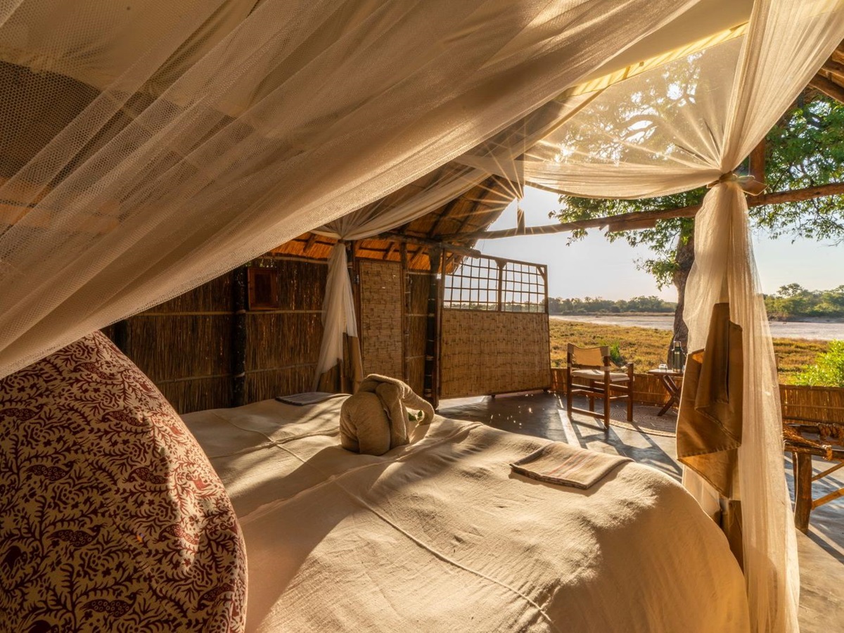 View from the double bed of a thachted room at luxury safari camp Luwi Bush Camp in Zambia over the private terrace and surroundings