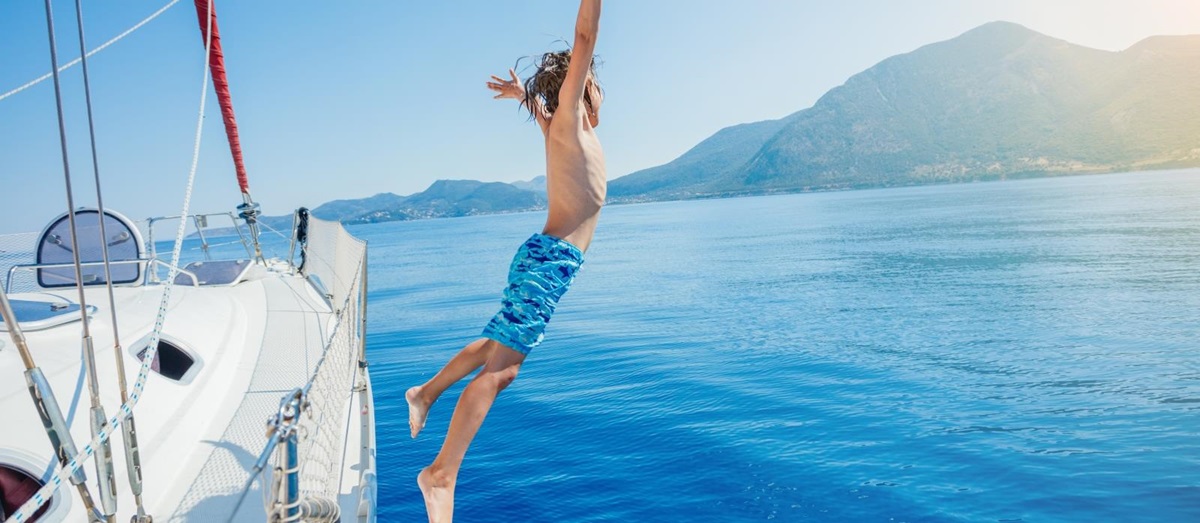 boy jumping of a sailing boat into blue water
