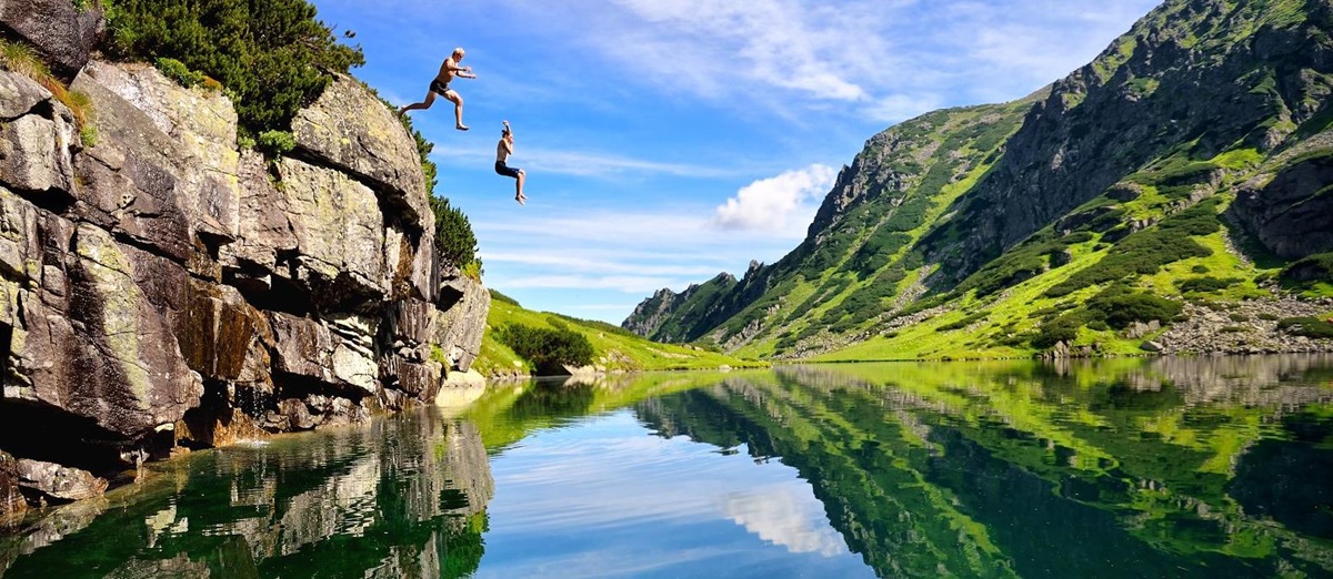 A couple jumping into a clear lake with mountain reflection