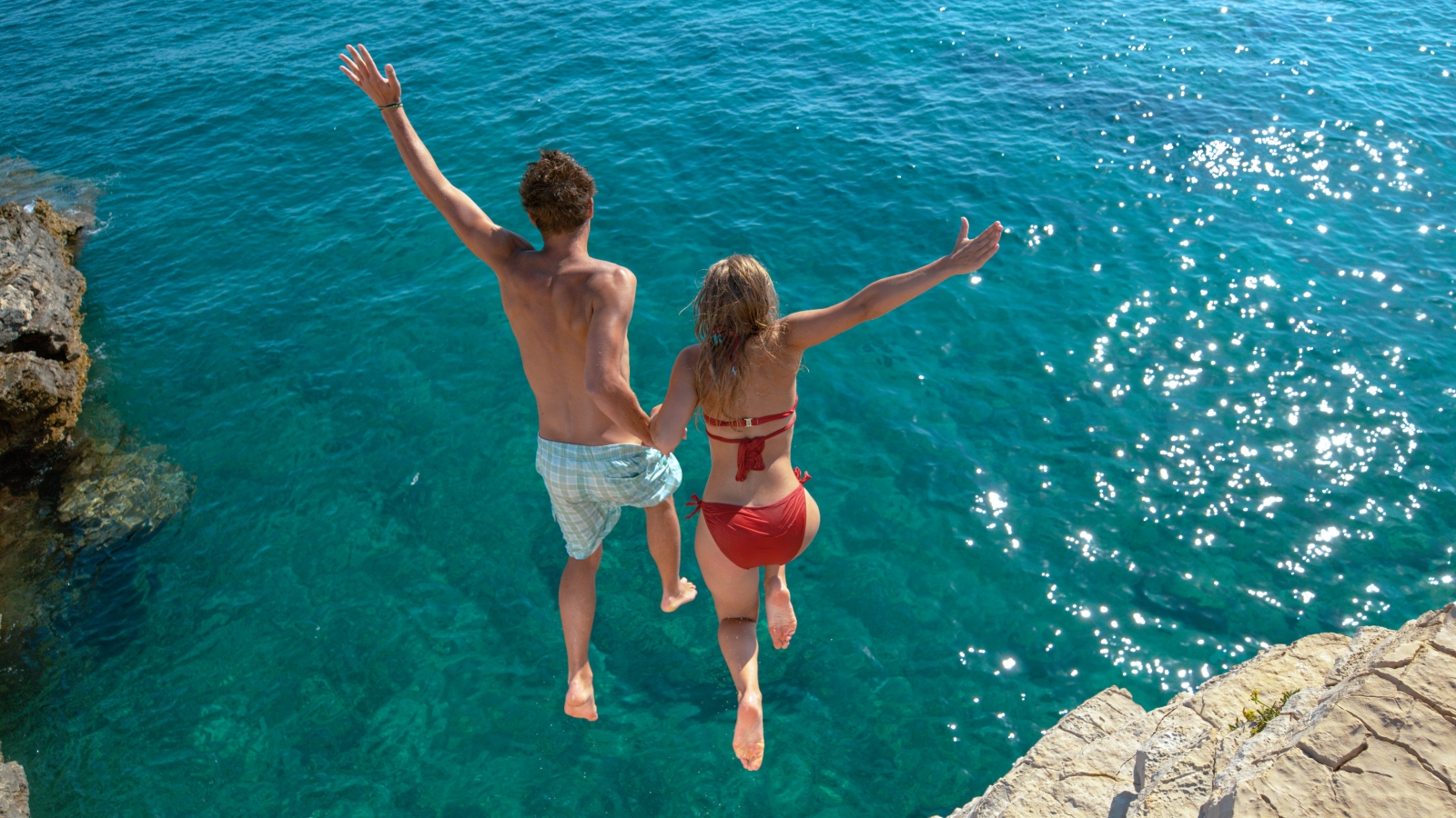 Couple jumping off a cliff into turquoise waters