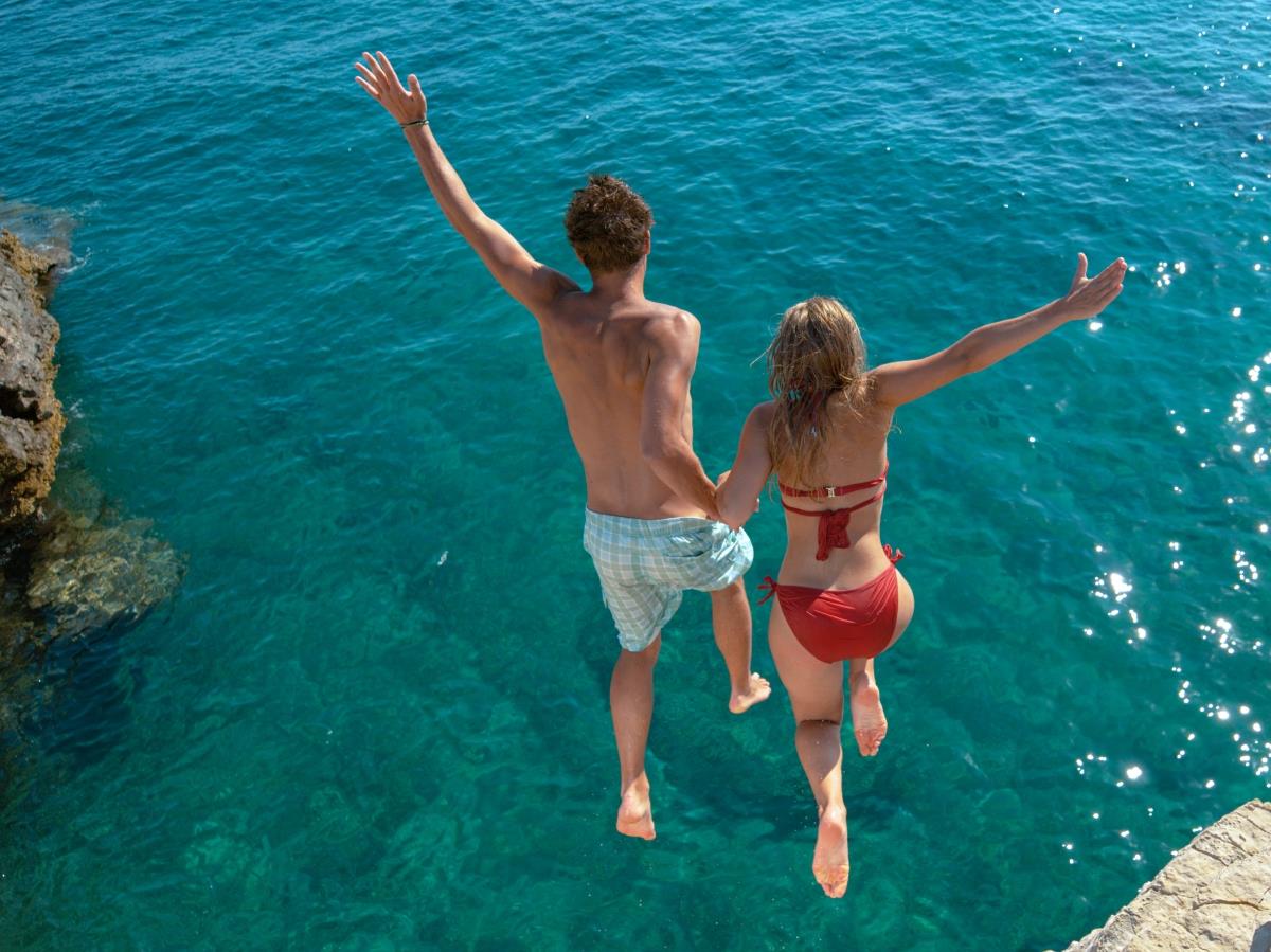 Couple jumping off a cliff into turquoise waters
